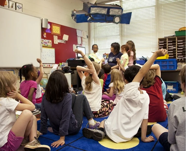 Educator with children in a classroom, hands raised